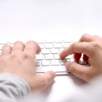 Des mains qui tapent sur un clavier d'ordinateur pour répondre à un questionnaire en ligne